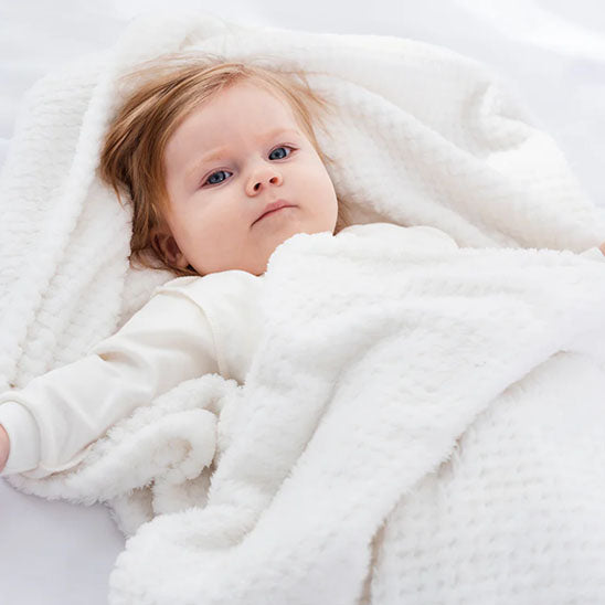 Bébé allongé sous une couverture bébé blanche moelleuse