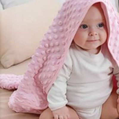 BĂ©bĂ© assis et souriant avec la couverture bĂ©bĂ© rose sur la tĂȘte
