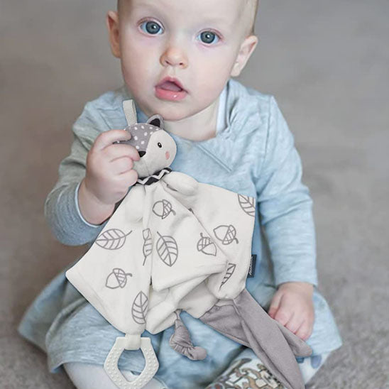 Bébé assise tenant un doudou renard blanc à motifs feuilles