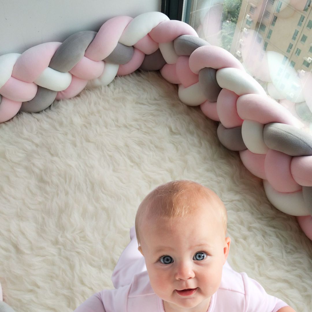 Bébé assis sur une moquette dans un tour de lit tressé rose poudré, blanc et gris