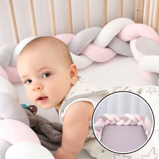 Bébé allongé contre un tour de lit tressé rose, blanc et gris dans un lit à barreaux