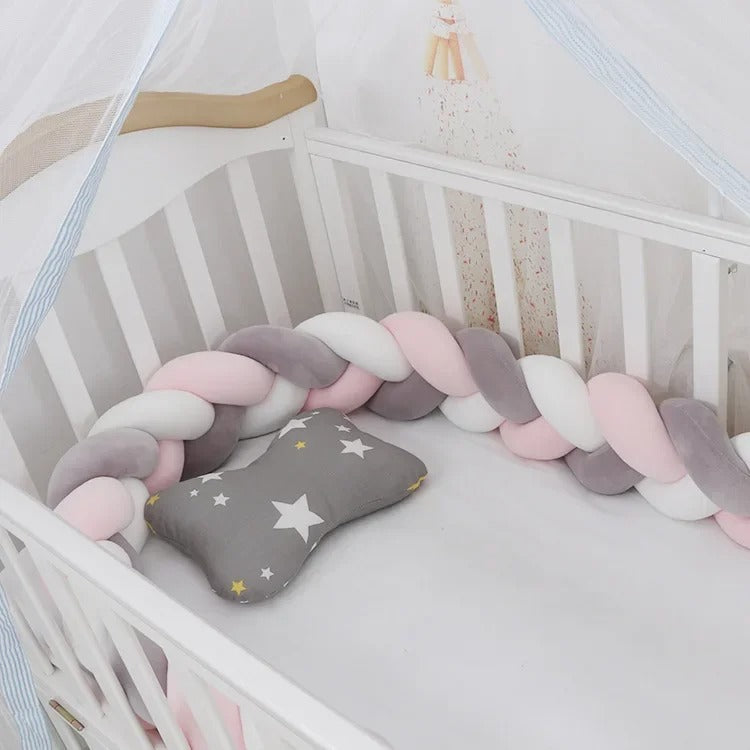 Tour de lit tressé rose, gris et blanc installé dans un lit bébé avec coussin étoilé