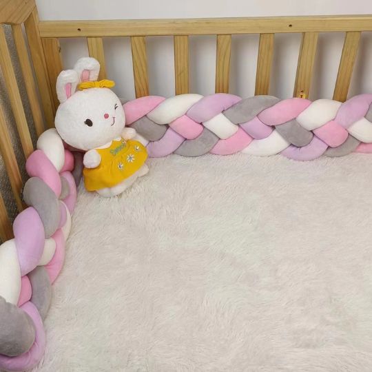 Tour de lit tressé rose, blanc et gris dans un lit en bois avec peluche lapin