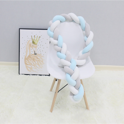 Tresse de lit bébé bleu ciel, blanc et gris posée sur une chaise blanche en déco douce