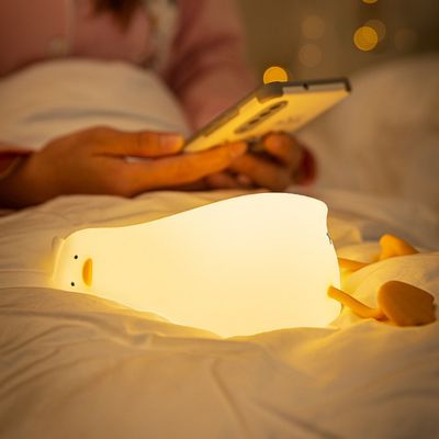 Veilleuse Lazy Duck à côté d'un smartphone dans un lit, offrant une ambiance apaisante