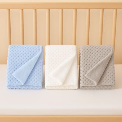 couverture bébé bleu blanc gris pliée sur matelas à barreaux