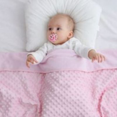 Bébé allongé avec tétine sous une couverture bébé rose