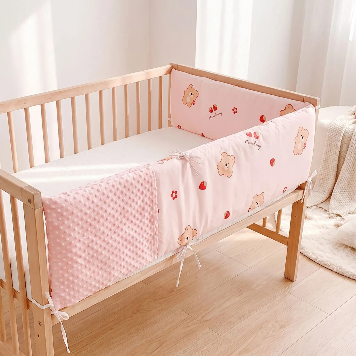 Tour de lit bébé rose installé autour d’un lit bébé en bois naturel