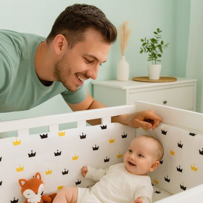 Papa sourit à bébé dans lit avec tour de lit couronnes