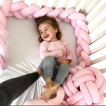 Enfant allongée et souriante dans un lit entouré d’un tour de lit tressé rose