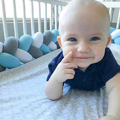 Bébé souriant allongé près d’une tresse de lit bébé bleu ciel, blanc et gris