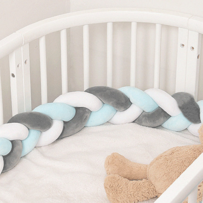 Tresse de lit bébé bleu ciel, blanc et gris installée dans un lit rond avec peluche